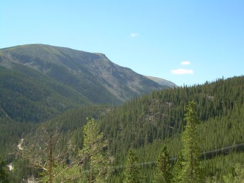 1996 Jeep Cherokee - A vast mountain scene unfolds with a winding road cutting through a dense forest under a bright blue sky.