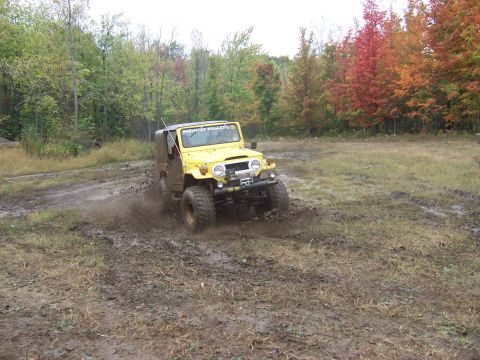 1978 Ford Bronco - A yellow Toyota Land Cruiser FJ40 with a soft top, round headlights and a front-mounted winch throws mud as it powers through a rutted mud…