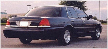 1999 Ford Crown Victoria - The rear of a dark-colored sedan is shown, distinctive taillights and chrome accents.