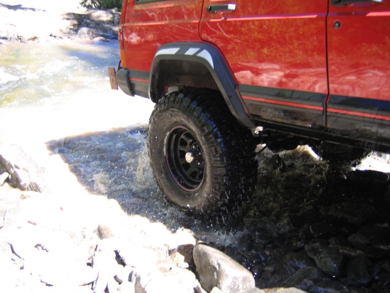 Front tire of a red Jeep Cherokee splashing through a rocky whitewater creek