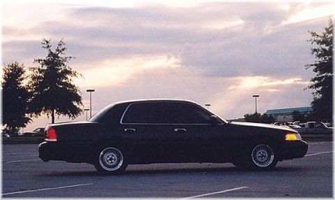 1999 Ford Crown Victoria - A dark sedan is parked in a lot under a cloudy sky.