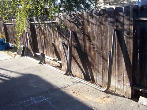1991 Ford Bronco - Metal tubing, likely for custom vehicle sliders, rests against a wooden fence.