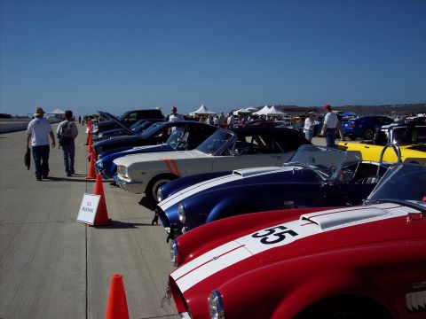 1971 Ford Mustang - Several classic sports cars are lined up on a sunny day, with spectators in the background.