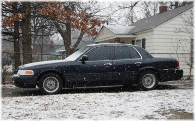 1999 Ford Crown Victoria - Dark sedan parked outside a house during a snowfall.