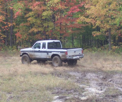 1990 Ford Ranger - A white 1990 Ford Ranger 4x4 navigates a muddy trail surrounded by colorful autumn foliage.