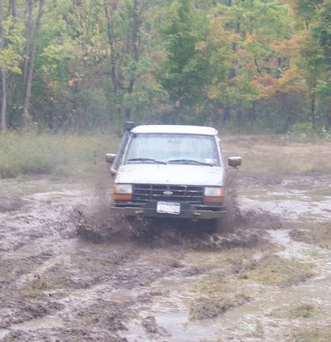 1990 Ford Ranger - A white 1990 Ford Ranger navigates a muddy off-road course, kicking up a large spray.