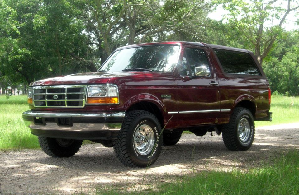 Red 1996 Ford Bronco parked on a dirt road with trees in the background