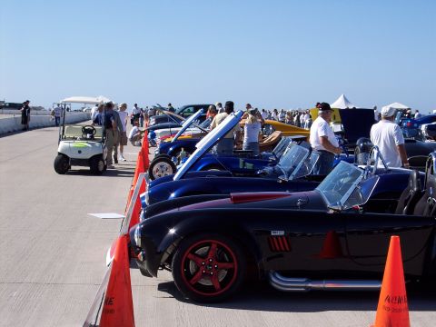 1971 Ford Mustang - A lineup of classic sports cars at an outdoor event, with a golf cart nearby.