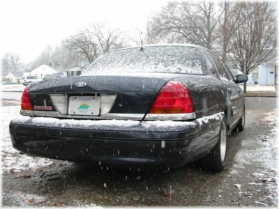 1999 Ford Crown Victoria - A dark sedan sits in the snow, viewed from the rear.