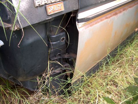 1979 Ford Bronco - Close-up of a rusty 1979 Ford Ranger XLT fender and door, partially obscured by grass.