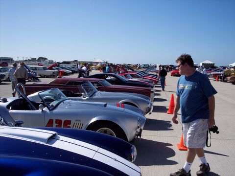 1971 Ford Mustang - A man walks past a row of classic cars on a sunny day.