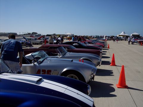 1971 Ford Mustang - A row of classic cars, including a silver convertible with '427' markings, are displayed outdoors under a clear blue sky.
