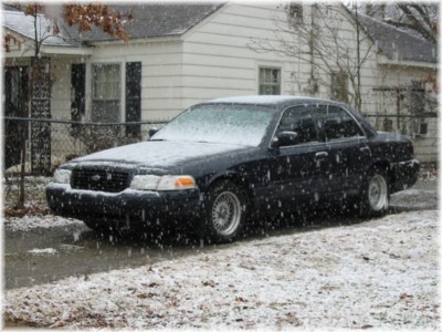 1999 Ford Crown Victoria - A black Ford Crown Victoria is seen parked in front of a house with snow falling around it.