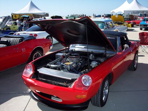 1971 Ford Mustang - A red convertible displays its engine at an outdoor car show, with other vehicles in the background.