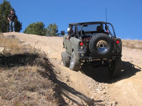 1995 Ford Bronco - Off-road vehicle navigates a steep dirt trail under a clear blue sky.