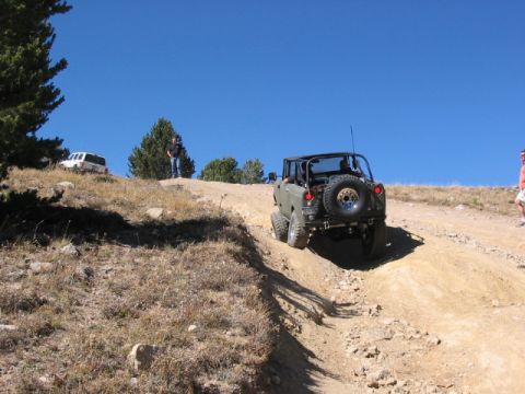 1995 Ford Bronco - Two vehicles navigate a steep, dry dirt trail under a clear blue sky.
