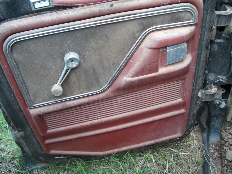 Maroon car door interior panel with chrome trim, manual window crank, and dusty texture