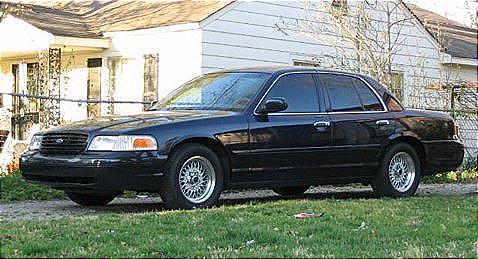 1999 Ford Crown Victoria - A black 1999 Ford Crown Victoria sedan is parked on a grassy lawn in front of a house.