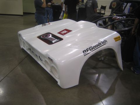1990 Ford Bronco - white fiberglass off-road race body shell bearing a BFGoodrich decal rests on a polished concrete floor at an indoor show.