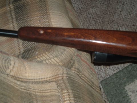 1919 Yugo Vega - The wooden stock of a rifle rests on a patterned blanket, with a scope visible underneath.
