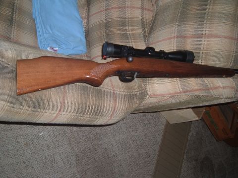 1919 Yugo Vega - A rifle with a scope rests on a plaid couch, with a blue shirt folded nearby.