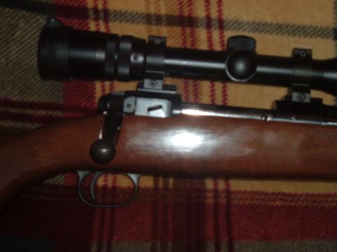 1919 Yugo Vega - A close-up view of a rifle's action and scope, set against a patterned fabric background.
