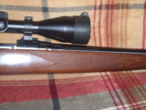 1919 Yugo Vega - Close-up view of a rifle with a scope mounted on top and a textured wooden stock.