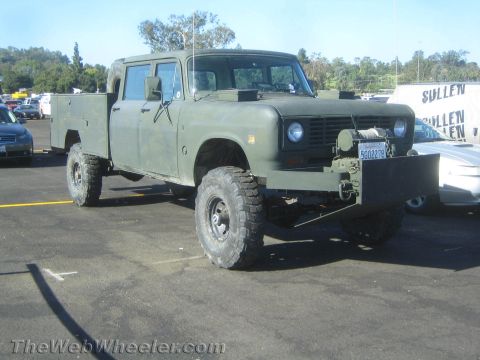 1990 Ford Bronco - olive-drab crew-cab 4x4 utility truck with a service bed, oversized off-road tires and a front-mounted winch parked on asphalt.