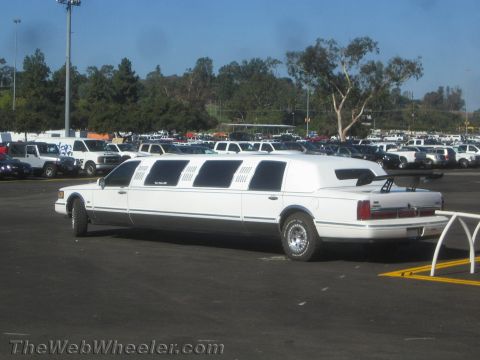 1990 Ford Bronco - white stretch limousine with multiple side windows and a vinyl-look roof parked in a crowded asphalt lot.