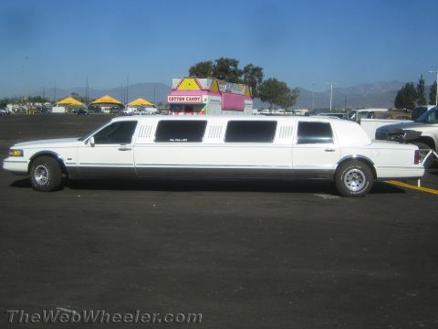 1990 Ford Bronco - Side profile of a long white stretch limousine parked on a dirt lot with a pink cotton-candy concession stand behind it.