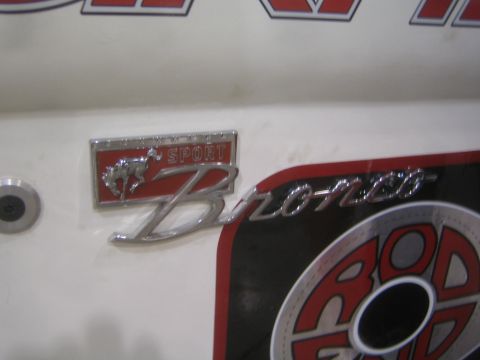 1990 Ford Bronco - Close-up of a chrome 'Sport Bronco' script badge with a small palm-tree graphic mounted on a glossy white body panel.
