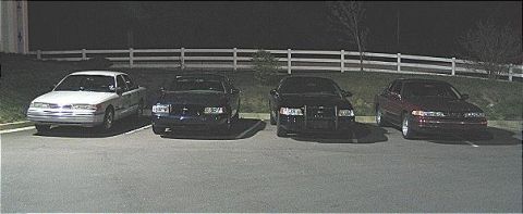 1999 Ford Crown Victoria - Several sedans are parked in a lot under artificial lighting at night.