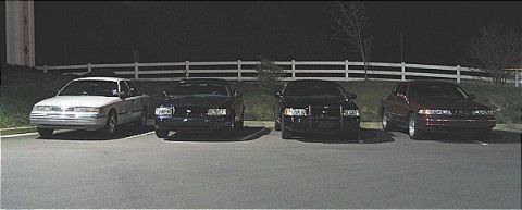 1999 Ford Crown Victoria - Four cars are parked in a lot at night, with the 1999 Ford Crown Victoria among them.