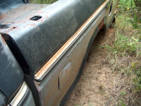 1979 Ford Bronco - The rear fender and tailgate area of a rusty 1979 Ford Bronco, showing signs of significant wear and tear.