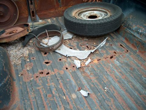 1979 Ford Bronco - The bed of a truck is filled with debris and a spare tire, showing significant rust damage.