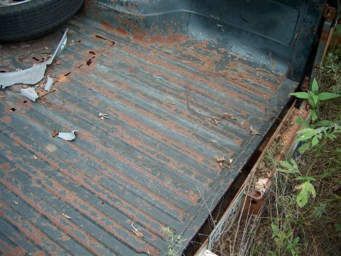 1979 Ford Bronco - The heavily rusted bed of a truck shows significant wear and tear, with a spare tire visible in the upper left corner.