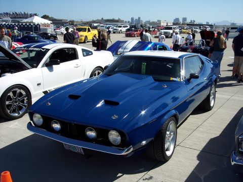 1971 Ford Mustang - A blue 1971 Ford Mustang with a white roof and hood scoops is parked at an outdoor car show.
