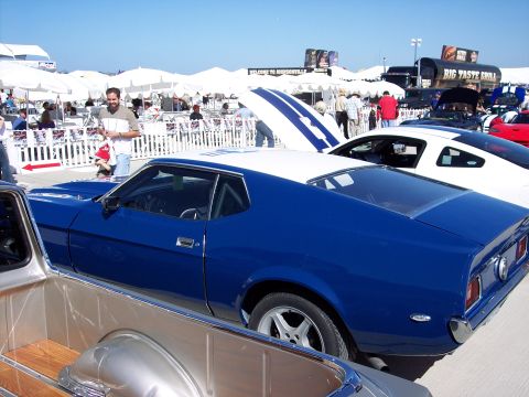 1971 Ford Mustang - A blue coupe with a white roof is parked at an outdoor event, with other vehicles and tents in the background.