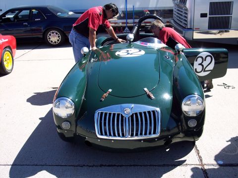 1971 Ford Mustang - Two men examine a green MG race car with prominent number 32 decals on the hood and door.