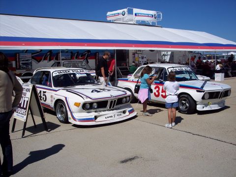 1971 Ford Mustang - Two vintage BMW race cars, identified by numbers 45 and 35, are displayed in front of a large tent structure.