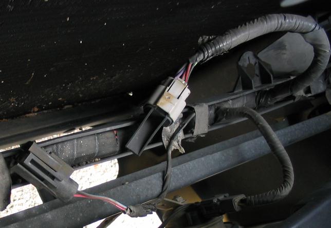 Close underbody shot of a taped wiring harness with two plug connectors under a vehicle