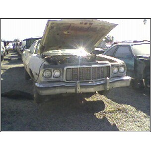 1973 Ford Ranchero - A 1973 Ford Ranchero sits in a junkyard with its hood open, showing its front grille and headlights.