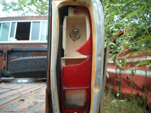 1979 Ford Bronco - Close-up of a damaged tail light on a weathered Ford F-Series truck, with another vehicle partially visible in the background.