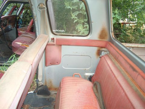 1979 Ford Bronco - The interior of an old vehicle shows signs of wear and tear, with faded red upholstery and visible rust.