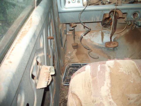 1979 Ford Bronco - The interior of a dilapidated 1978 Ford Bronco reveals its worn-out door panel, rusted pedals, and tattered seat.