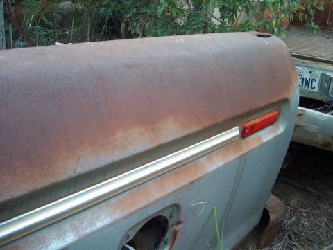 1979 Ford Bronco - This close-up shows a heavily rusted vehicle panel with a red side marker light and a strip of chrome trim.