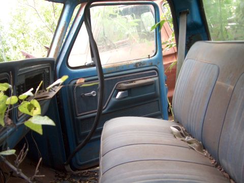 1979 Ford Bronco - The interior of a weathered blue 1973 Ford F-Series truck cab, showing a dusty bench seat and door panel.