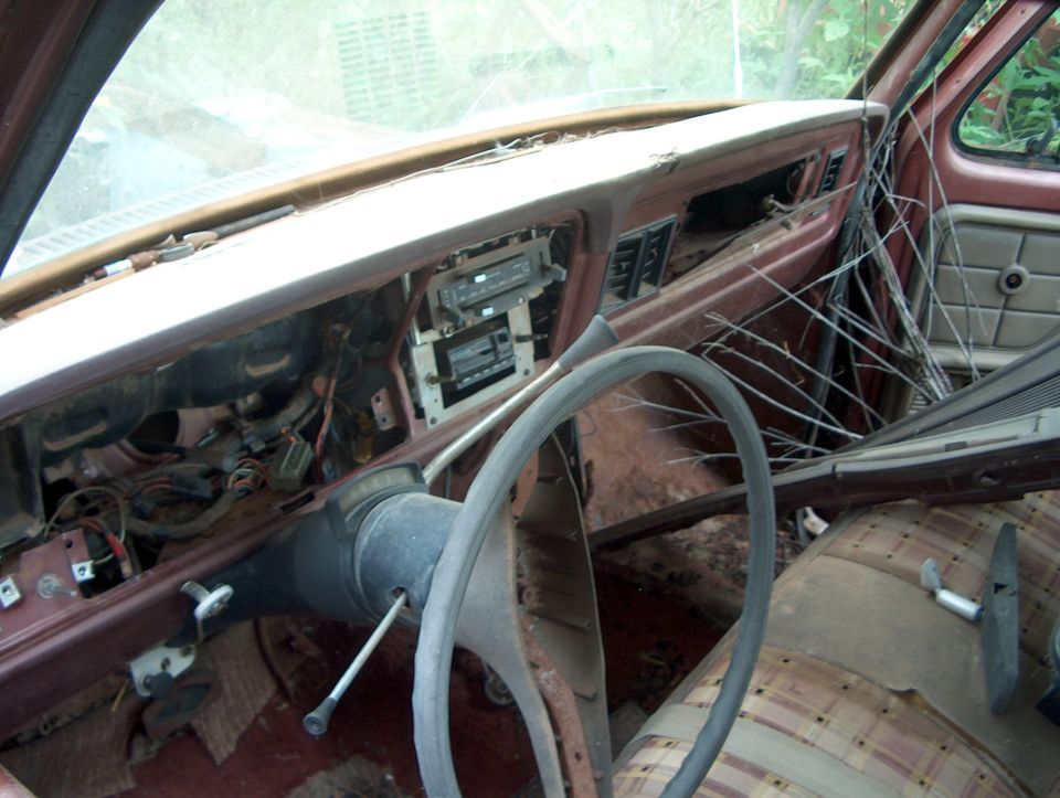 Interior of a beat-up vehicle, showing dashboard, steering wheel, and plaid seats