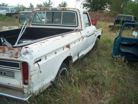1979 Ford Bronco - This old pickup truck is sitting in a junkyard with several other vehicles around it.