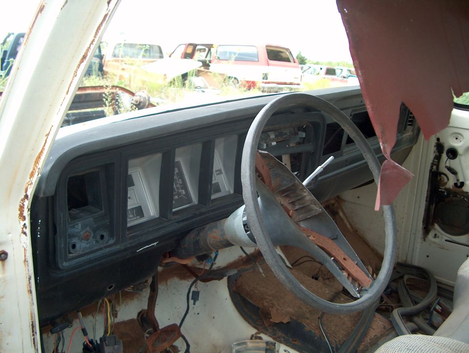 1979 Ford Bronco interior showing dashboard, steering wheel, and gauges. Other vehicles visible in background